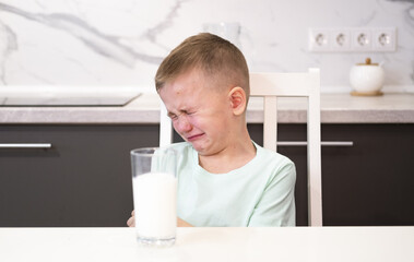 An unhappy child refuses to drink milk for breakfast and sits in kitchen without an appetite. Upset...