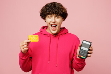 Young Caucasian man he wearing hoody casual clothes hold wireless modern bank payment terminal to process acquire credit card isolated on plain pastel light pink background studio. Lifestyle concept.