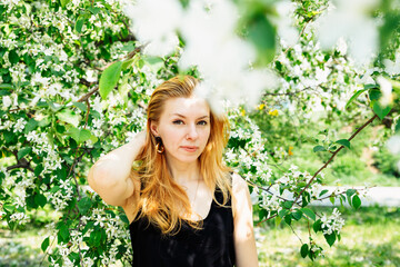 woman portrait in apple blossom tree. 39 year old white caucasian female with long yellow red hair. spring summer lifestyle waist up portrait, looking at camera. loneliness, sadness, alone