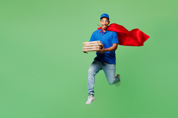 Full body delivery guy employee man wear blue cap t-shirt uniform workwear red super hero cloak work dealer courier hold cardboard box jump high run isolated on plain green background Service concept