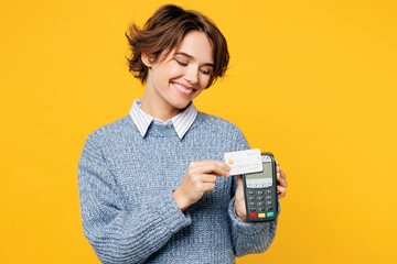 Young woman she wears grey knitted sweater shirt casual clothes hold wireless modern bank payment terminal to process acquire credit card isolated on plain yellow background studio. Lifestyle concept. - obrazy, fototapety, plakaty