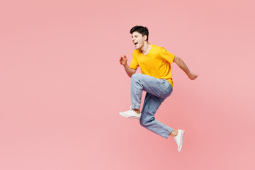 Fototapeta na wymiar Full body side view cool fun overjoyed young man he wears yellow t-shirt casual clothes jump high run fast hurry up isolated on plain pastel light pink background studio portrait. Lifestyle concept.