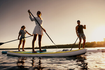 Group of happy sporty friends are relaxing and walking with stand up paddle sup boards at sunset...
