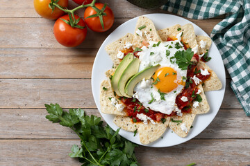 Traditional Mexican breakfast red chilaquiles with egg on wooden table. Top view. Copy space