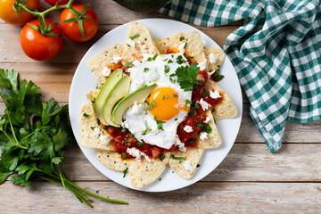 Traditional Mexican breakfast red chilaquiles with egg on wooden table. Top view