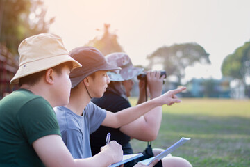 Asian teenboys learning nature by using binoculars to watch birds and insects in public park during...