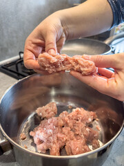 Female hands make meatballs with red fat mince, close up