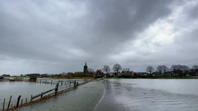 IJssel river flood at Wilsum village with water running over the road through floodplains during flooding caused by high water levels after heavy rain.