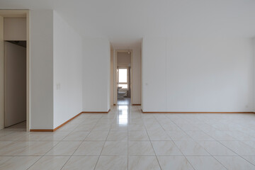 Empty room with tiles and white walls. The door is open to the bathroom