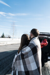 Fototapeta premium A couple in love is having a romantic date while traveling. A man and a woman are posing against the backdrop of snowy mountains, drinking tea. Travel concept