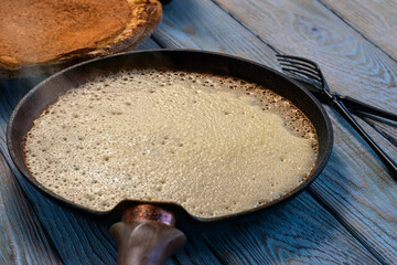 Thin pancake in pancake pan, toasted on one side. Steam rises from the pancake. Traditional Russian dish