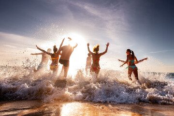 Large group of happy young friends are having fun and runs to swim at sunset sea beach. Tropical...