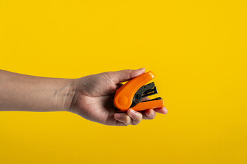 Orange stapler in hand isolated on yellow background
