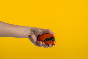 Orange stapler in hand isolated on yellow background

