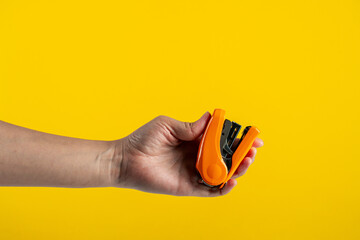 Orange stapler in hand isolated on yellow background
 - obrazy, fototapety, plakaty