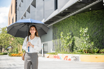 Walking to the office on a scorching day, a young businesswoman holds an umbrella to shield herself...