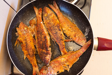 Fried fish in a frying pan on a gas stove in the kitchen