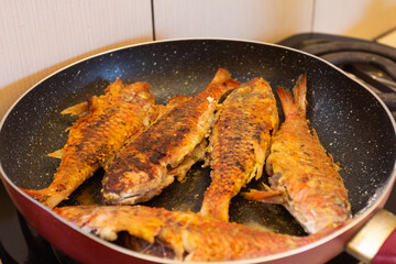 Fried fish in a frying pan on a gas stove in the kitchen