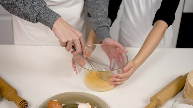 Teenage children whisking egg in bowl with metal wire whisk close up. Kids pastry chef preparing dough. Cooking process cookies and pastry