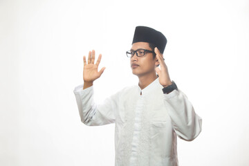 Asian Muslim man in white koko shirt performing prayer and both hands raised standing isolated white studio, Muslim man concept