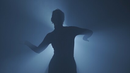 Female model against bright backlight on black smoky background in studio. Female silhouette,...