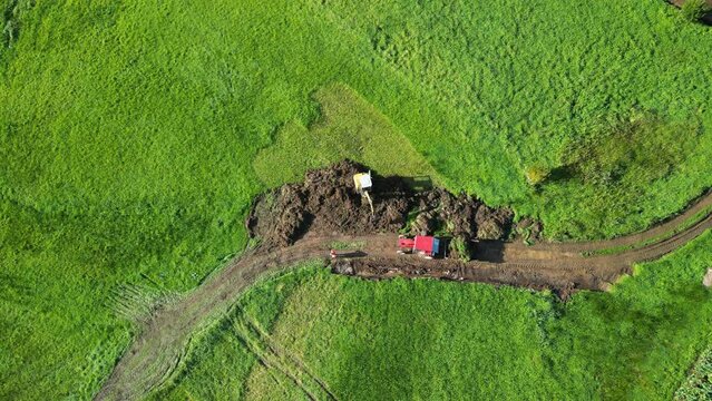 Rotating aerial footage of long-arm excavator digging soil on green field in Zas, A Coruna, Spain