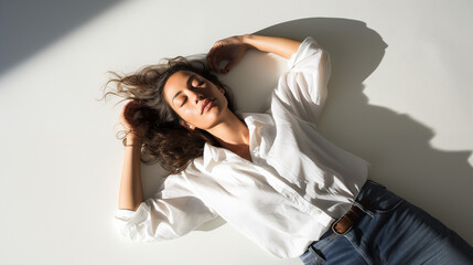 Naklejka premium Casual and tranquil mood captured as a woman lies in repose on a white surface, with the interplay of light and shadow adding depth