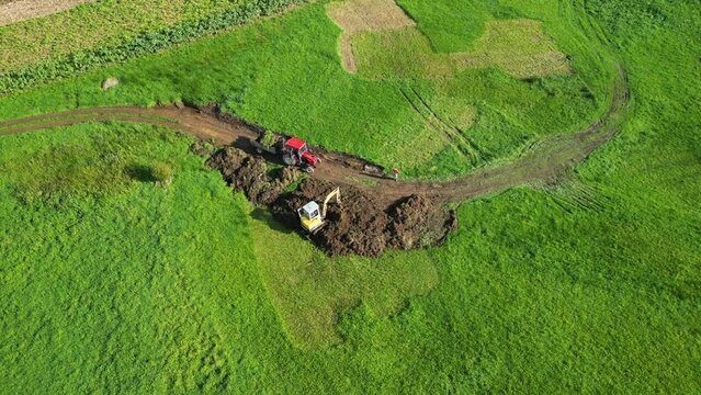 Aerial footage of a backhoe loader scooping the soil in a green field in Zas, A Coruna, Spain