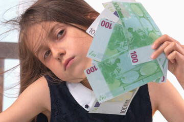 Conceptual image: Teaching kids about money. Close up portrait of young beautiful girl working online and counting US Dollar money. Horizontal image.