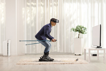 Full length profile shot of a businessman skiing on a carpet with a VR headset in front of a tv
