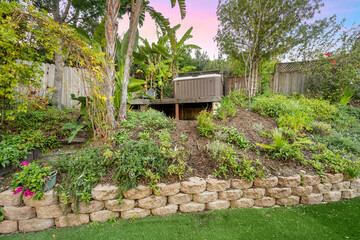 Stone wall with shrubs and trees adjacent to a fenced-in backyard