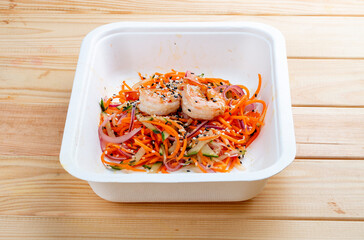 Korean-style salad with shrimp, fresh vegetables and spicy carrots. Healthy food. Takeaway food. On a wooden background.
