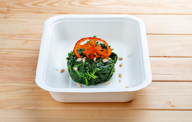 Braised spinach with pine nuts. Healthy food. Takeaway food.  On a wooden background.