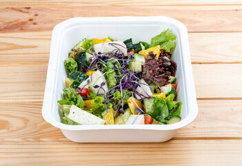French salad with Camembert cheese. Healthy food. Takeaway food.  On a wooden background.