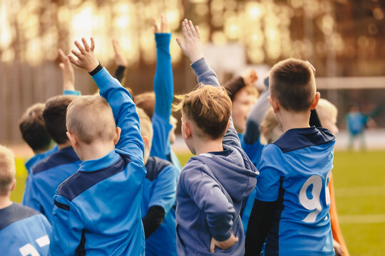 Children's sports team standing in a circle and rising hands up. Kids play sports match. School boys in blue jersey shirts huddling in a team. School sports team compete in a game