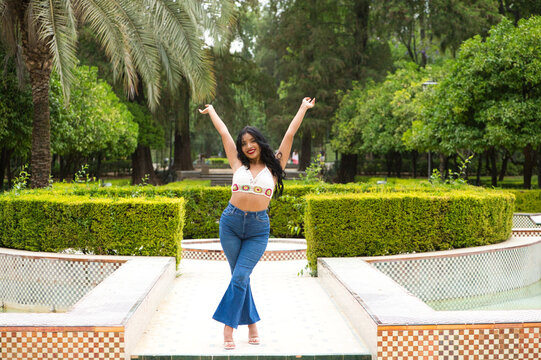 Young and beautiful brunette woman and latin, walks among the trees and vegetation of the park and raises her arms. The woman smiles and is happy. Concept happiness and yellow day
