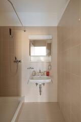 Detail of a sink with soaps on it and a shower with a curtain. There are tiles on both the floor and the walls.