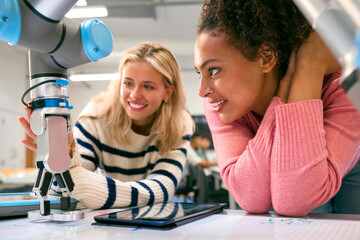 Two Female College Or University Engineering Students Using Digital Tablet To Control Robot Arm