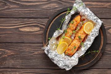 Baked salmon infoil with lemon on wooden background. Mediterranean diet concept. Copy space