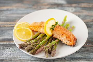 Baked salmon with asparagus and lemon on gray wooden background. Mediterranean diet concept. Copy...