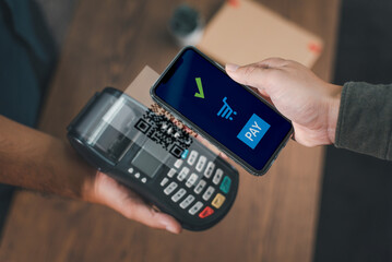 Close-up of a hand holding a smartphone completing a payment transaction at a point of sale terminal.. - obrazy, fototapety, plakaty