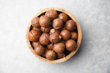Delicious macadamia nuts in bowl on light grey table, top view