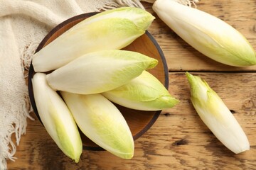 Fresh raw Belgian endives (chicory) and bowl on wooden table, top view