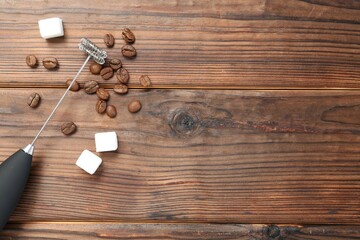 Black milk frother wand, sugar cubes and coffee beans on wooden table, flat lay. Space for text