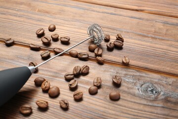 Black milk frother wand and coffee beans on wooden table, closeup