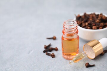 Clove oil in bottle, pipette and dried buds on grey table, closeup. Space for text