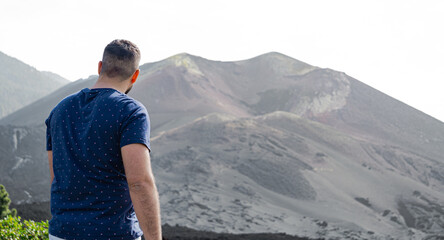 man from behind and standing, looking at the crater of a volcano - obrazy, fototapety, plakaty
