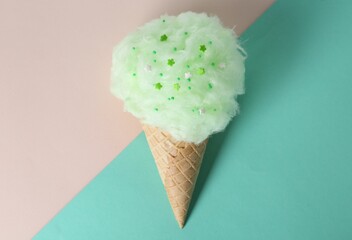 Sweet cotton candy in waffle cone on color background, top view