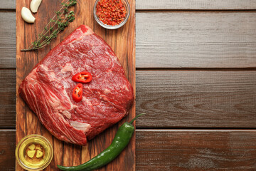 Fresh raw beef cut, spices and oil on wooden table, top view. Space for text