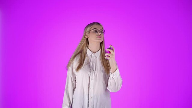 Modelka na r&oacute;żowym tle delikatnie psika się perfumami na szyję i koszulę. Uśmiechnięta, elegancka, zmysłowa &ndash; ujęcie beauty ukazujące codzienny rytuał zapachu i kobiecej subtelności